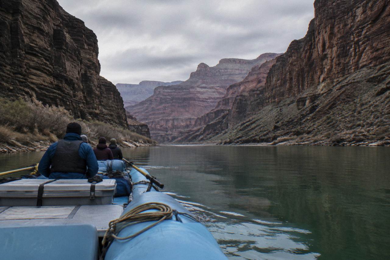 A motorized raft floating on calm green water between dark canyon walls