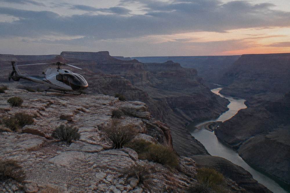 A helicopter parked on a rocky ledge above a river winding through a desert canyon