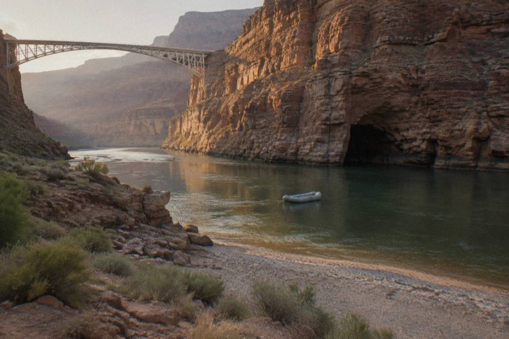 A raft drifting on emerald green water near a cave entrance in a canyon wall