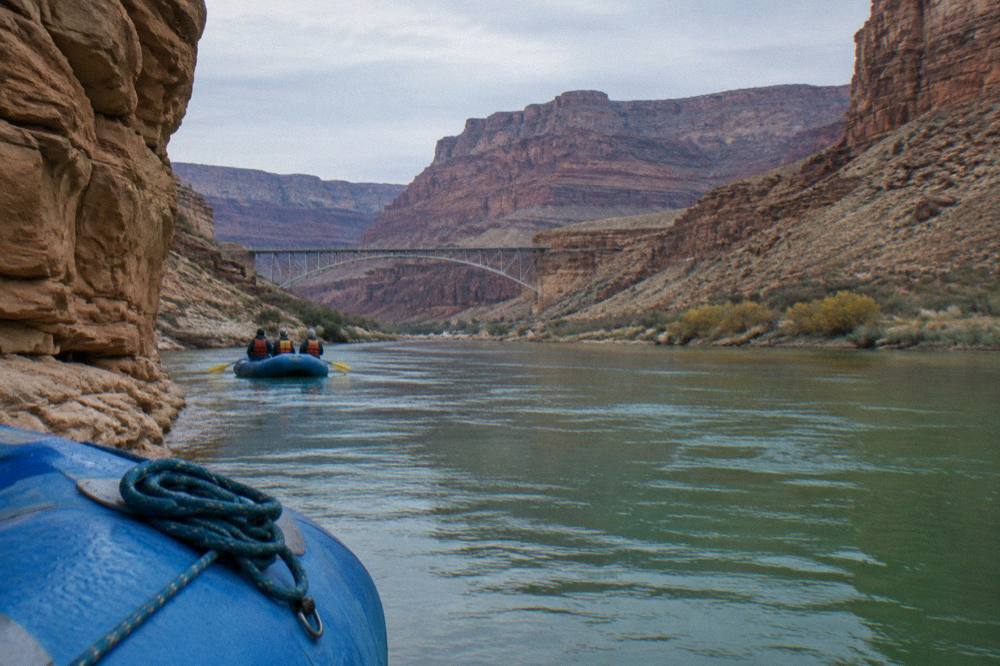 A group of people in life vests riding a raft on calm water through a deep canyon