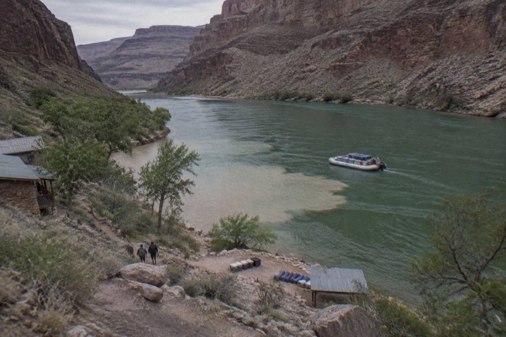 Large motorized raft loaded with camping gear floating on a wide green stretch of the Colorado River