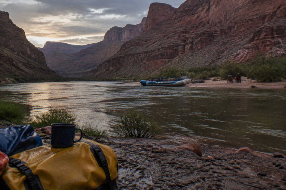 Camped raft on a sand beach beside the river with red canyon walls rising behind