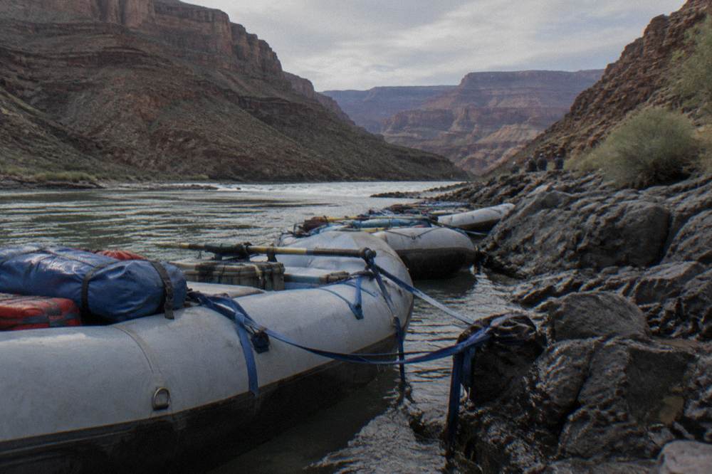 Row of oar rafts tied at a rocky river bank in late afternoon light