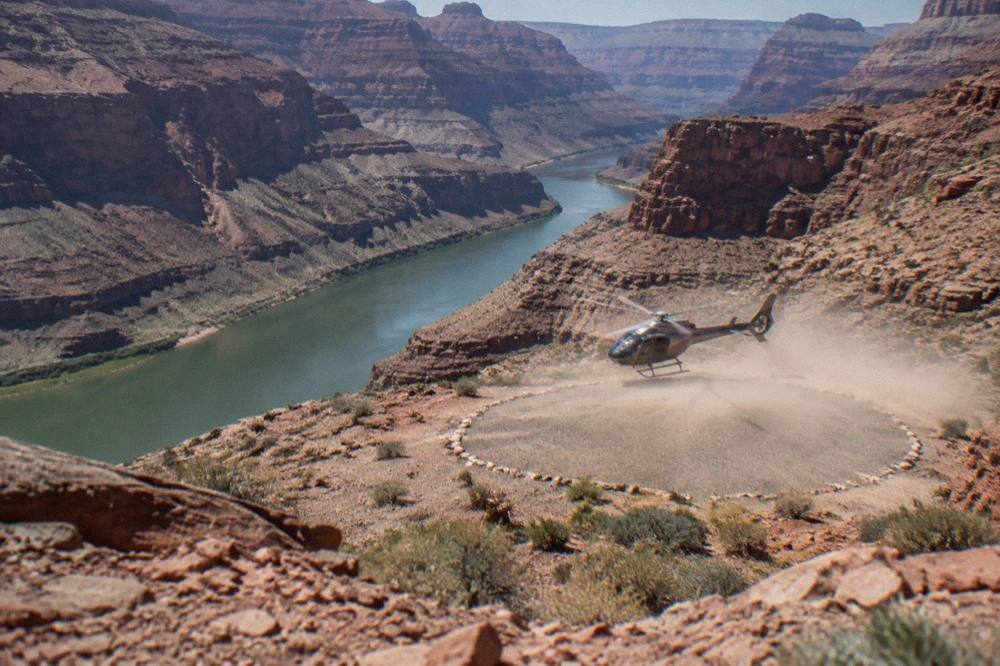 Helicopter lifting off from a canyon floor landing zone beside the river