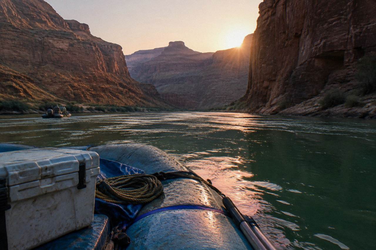 Motorized raft drifting between dark canyon walls on the Colorado River at sunrise