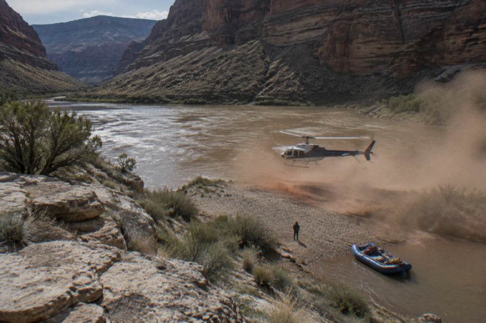 A helicopter lifting off from a gravel bar beside a river inside a deep canyon