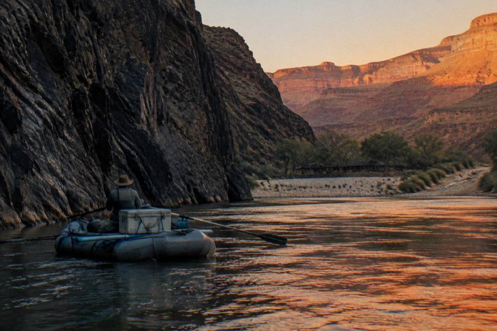 A raft on a river in late afternoon light below dark canyon walls