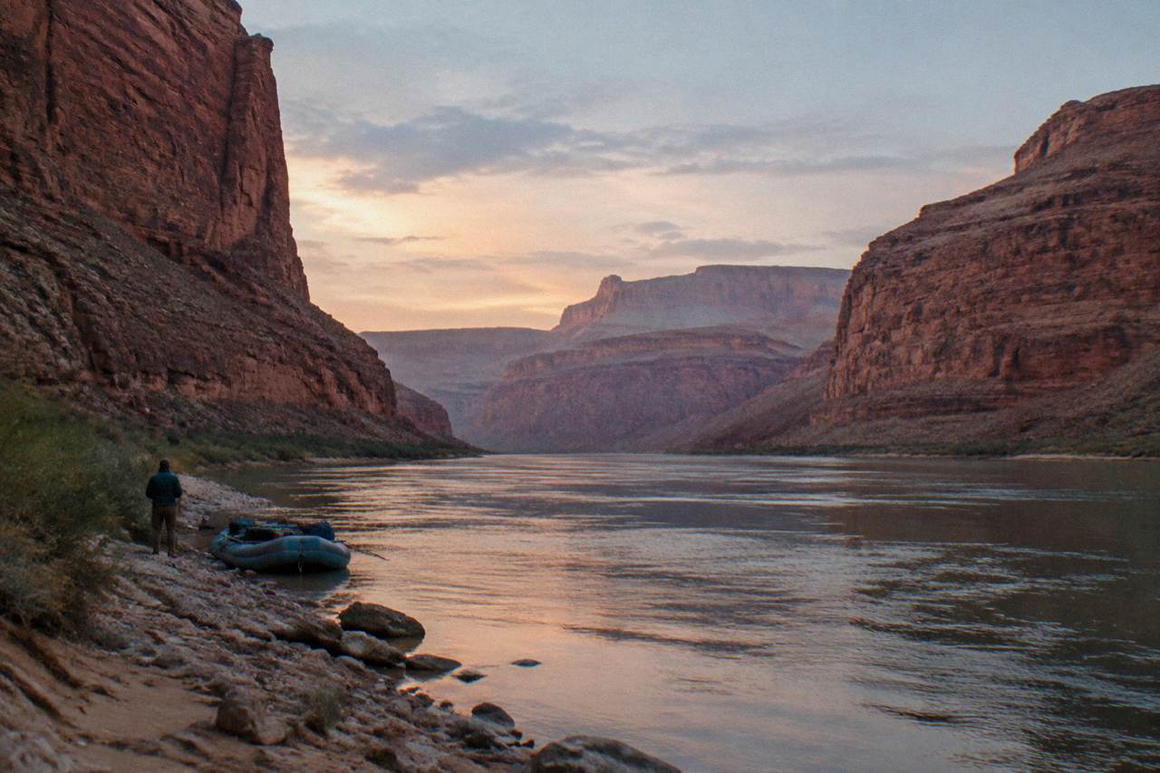 A calm stretch of the Colorado River between tall red canyon walls under a wide sky