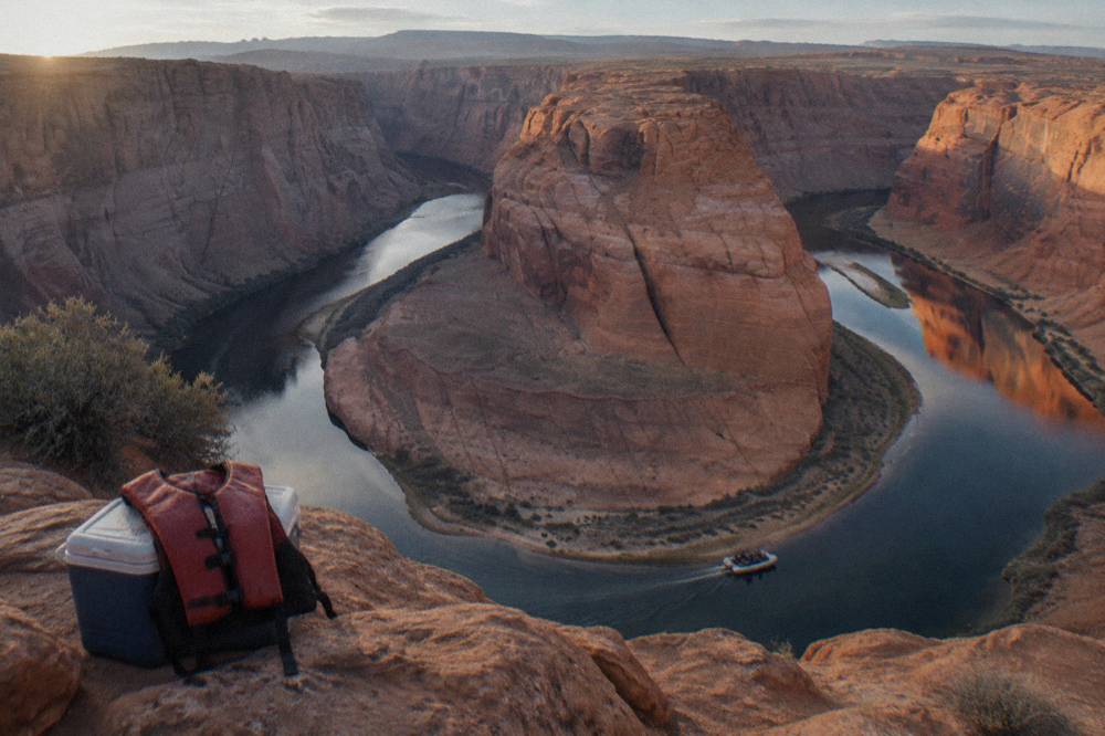 A motor raft carrying passengers along a wide calm river bend beneath orange sandstone cliffs