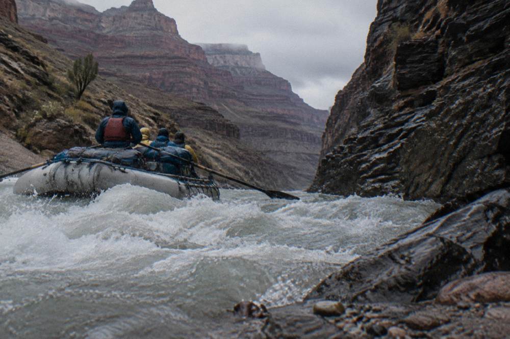 A whitewater raft cutting through a foamy rapid between dark canyon walls