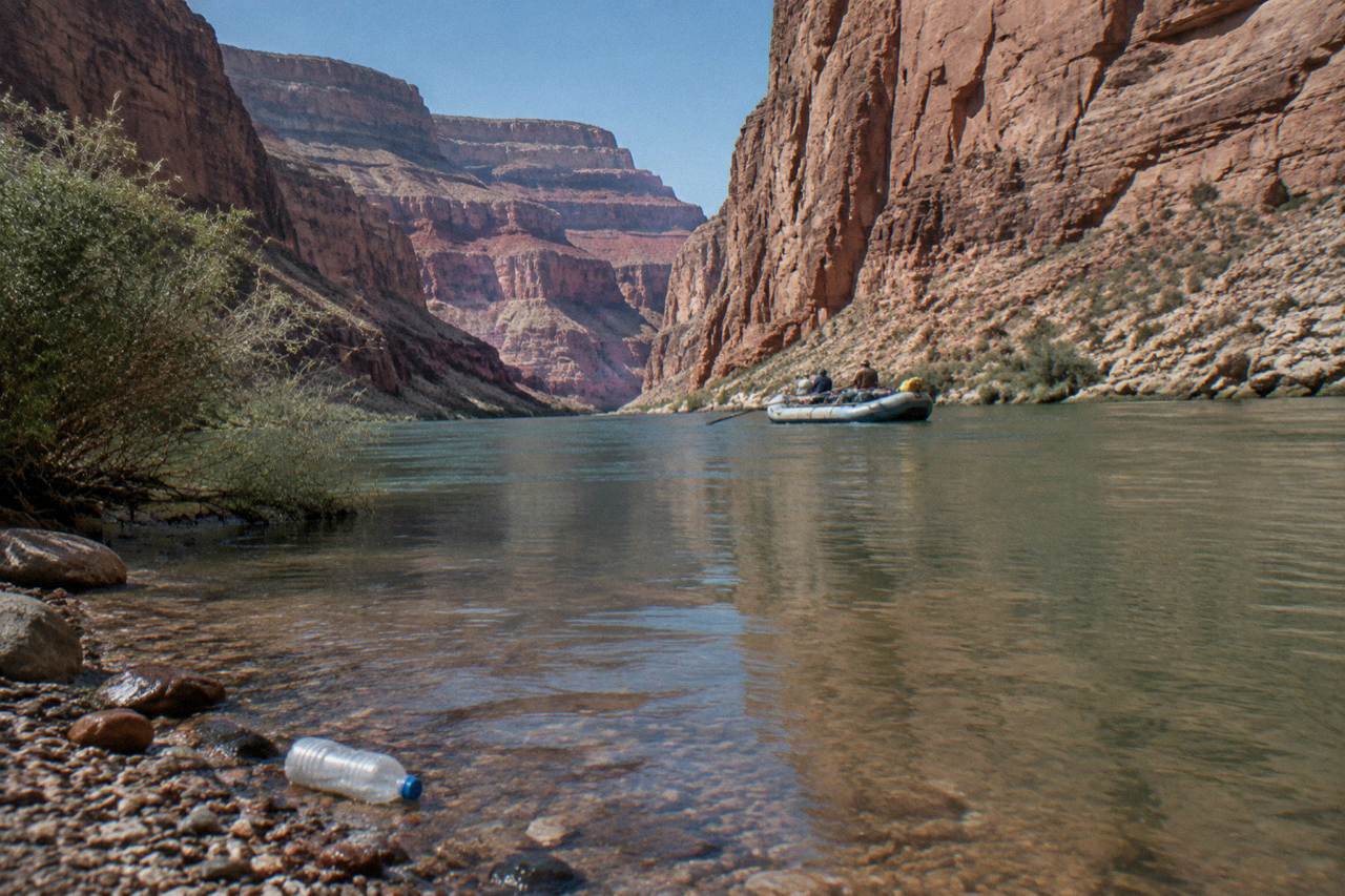 A raft drifting on calm green water between steep canyon walls in bright sunlight